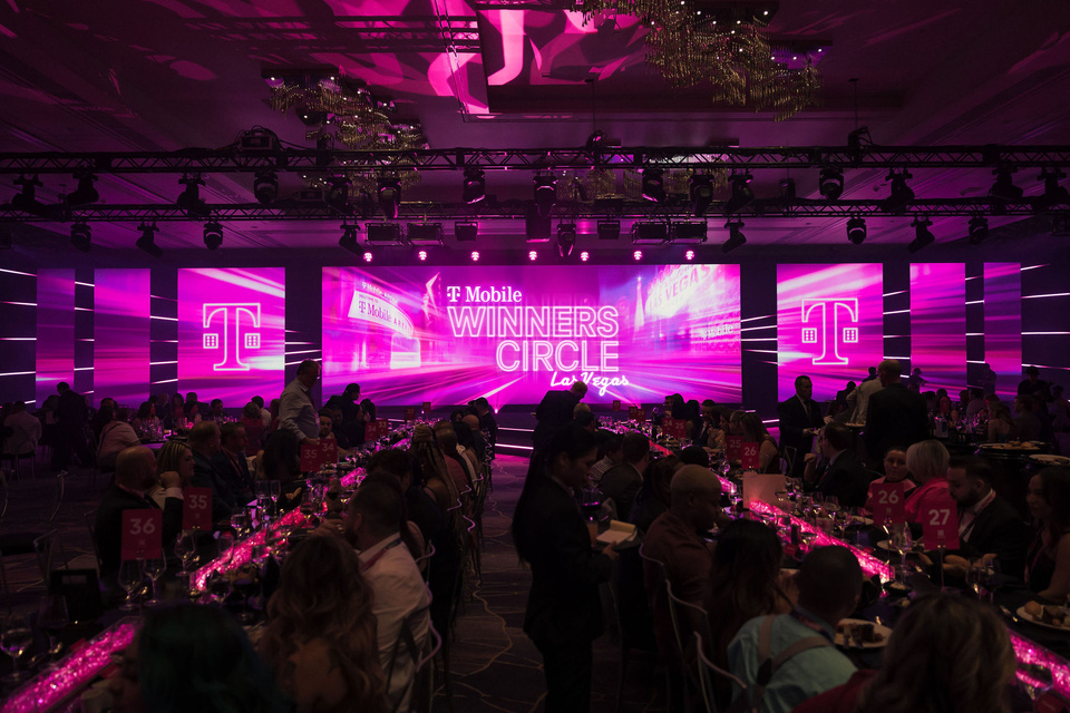 Photo of attendees at long tables in front of LED screens showing T-Mobile Winners Circle 2022 Las Vegas branding