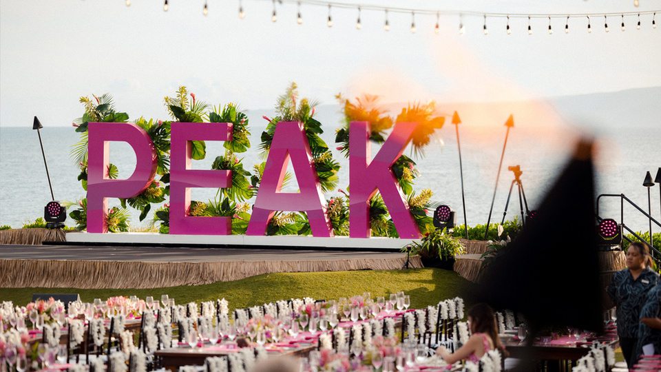 Photo of Hawaii landscape with large magenta PEAK letters as a backdrop to a dinner set