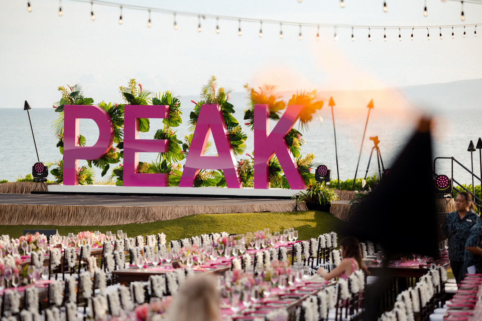 Photo of Hawaii landscape with large magenta PEAK letters as a backdrop to a dinner set