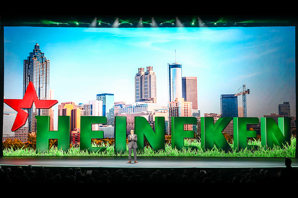 Photo of presenter on stage in front of Heineken branding and a cityscape on an LED screen