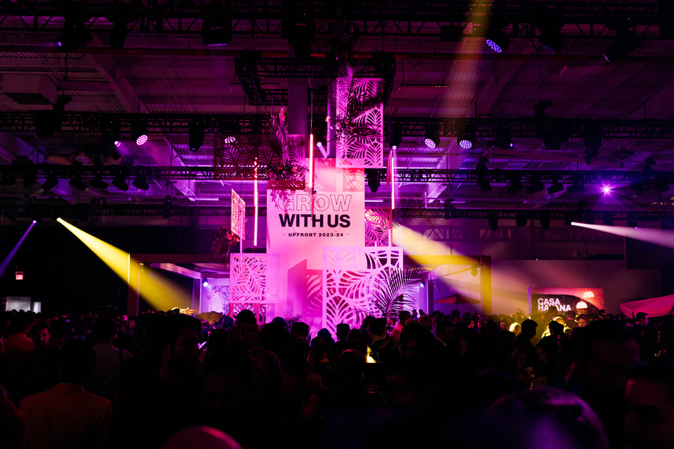Photo of crowd looking at centerpiece reading Grow with Us Upfront 2023-2024. Scene has pink lighting