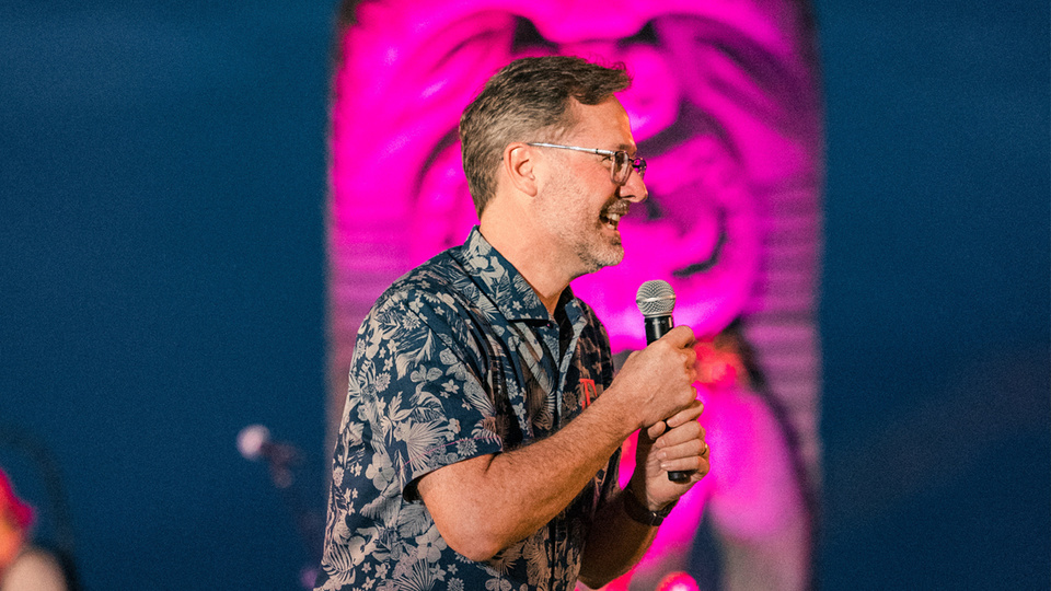 Photo of man on stage holding a microphone in a Hawaiian shirt