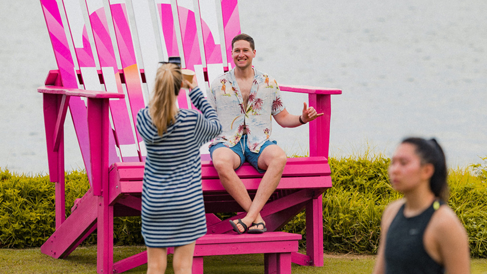Photo of woman taking a photo of a man seated in an oversized magenta Adirondack chair with T-Mobile branding