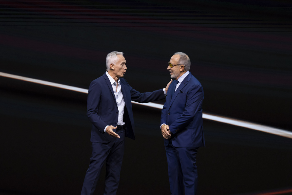 Photo of 2 men in conversation on a stage, with one man putting his hand on the other's shoulder.