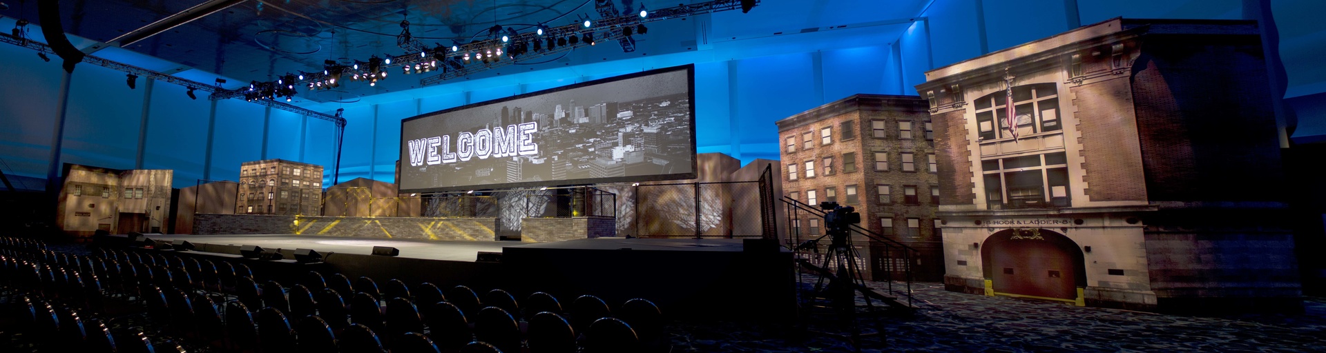 Photo of a city themed set with a screen that says welcome. Stage and audience are empty