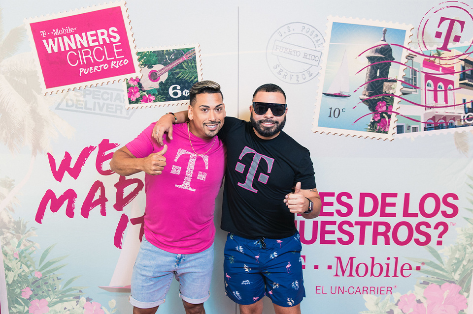 Photo of 2 event guests posing in front of a T-Mobile Winners Circle Puerto Rico photo step and repeat giving a thumbs up.