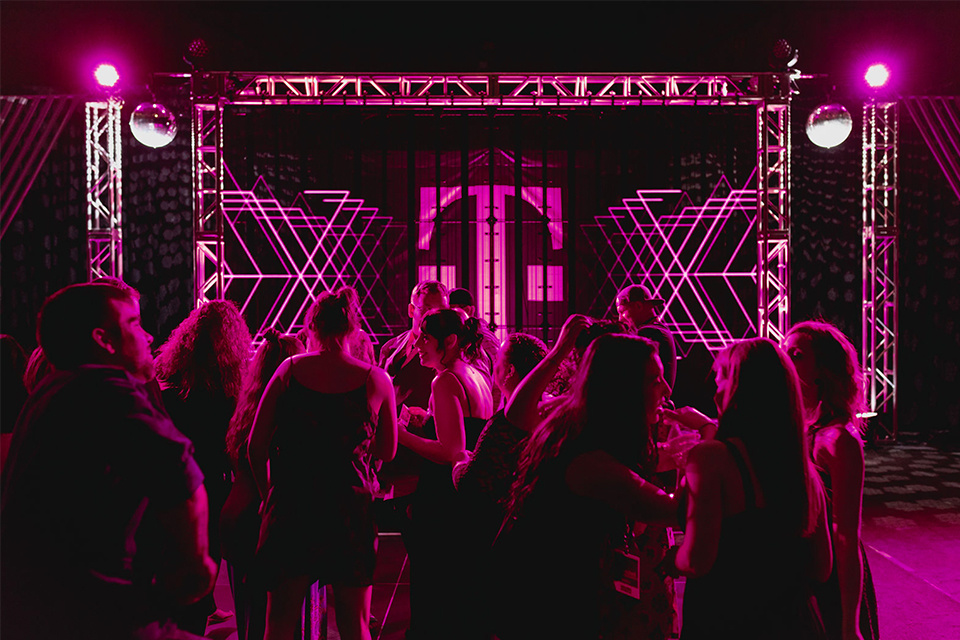 Photo of a group of around 20 event attendees standing in front of a magenta lit stage with the T-Mobile logo