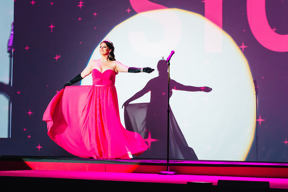 Photo of performer on stage signing while wearing a magenta dress