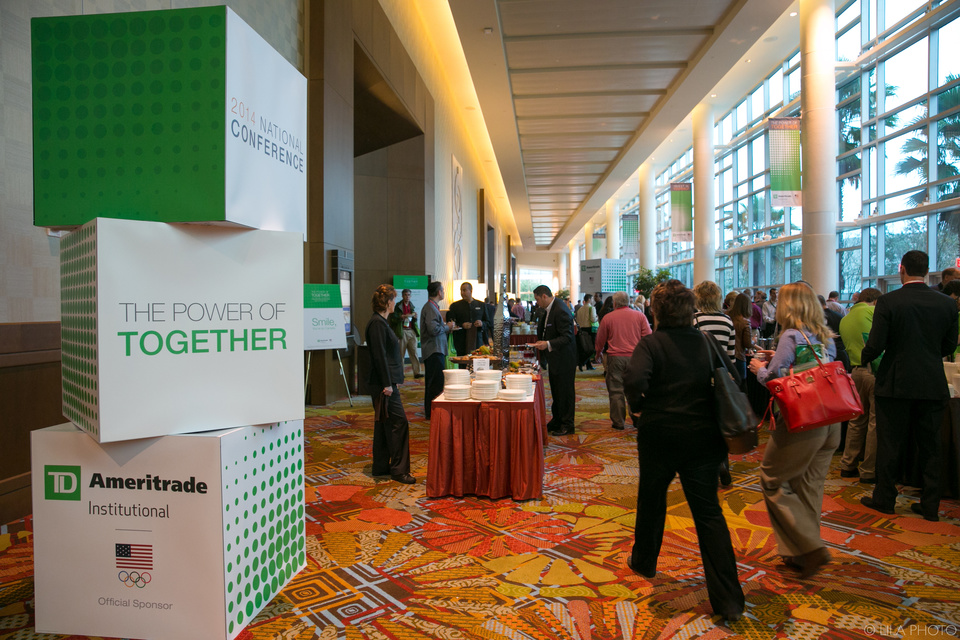 Photo of many people walking through a Catering area Outside of a ballroom with TD Ameritrade Institutional branding in the foreground that reads "The Power of Together."