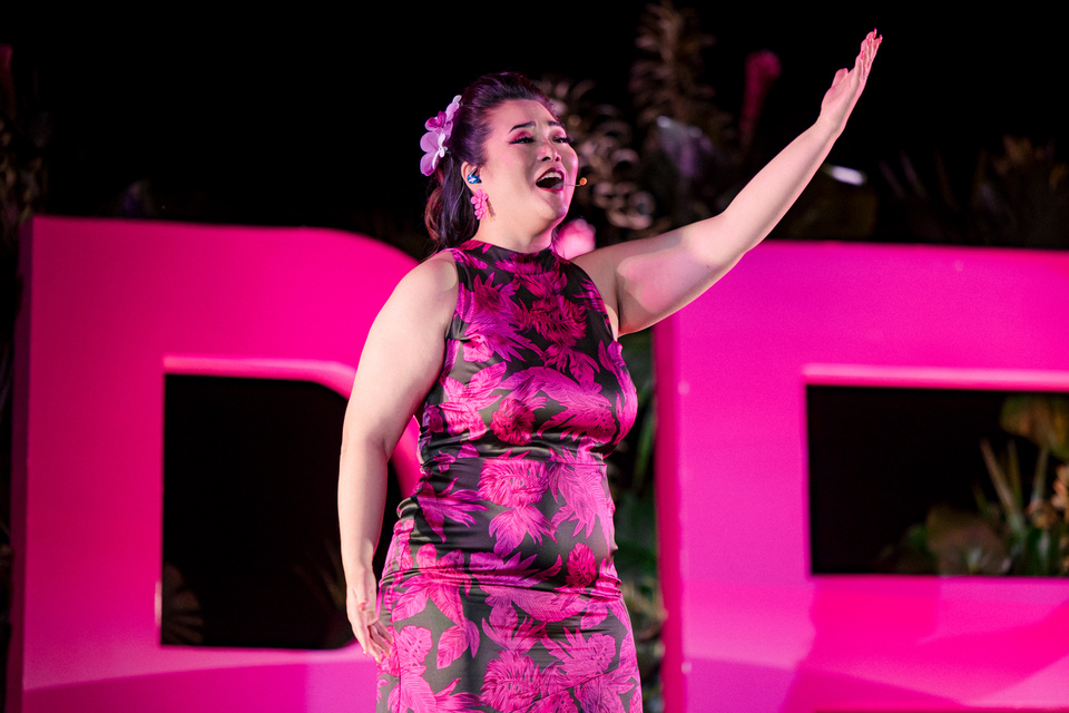 Photo of a performer on stage singing with one arm in the air.