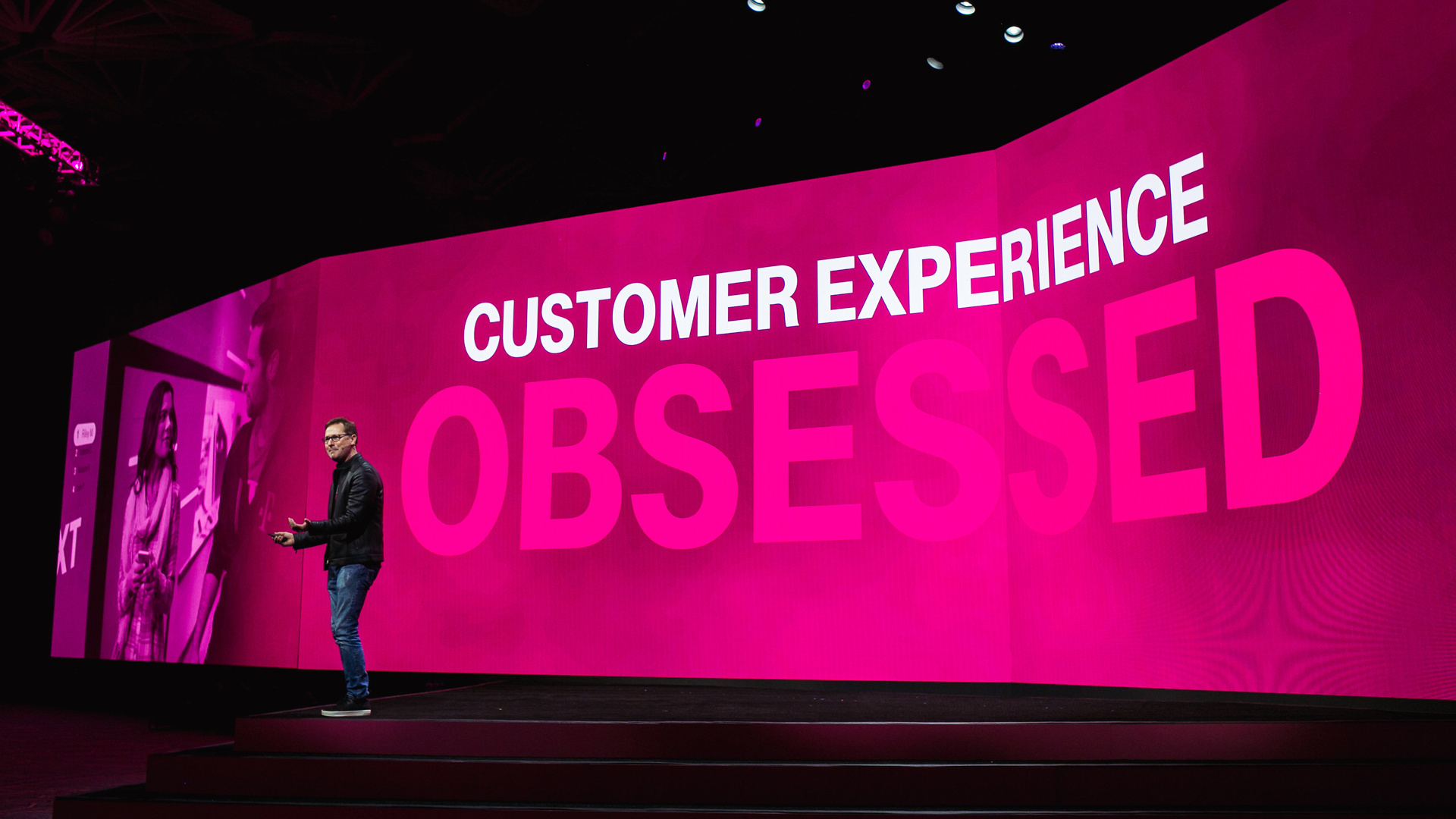Photo of presenter on stage in front of a Magenta screen that reads "Customer experience obsessed."