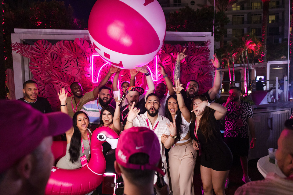 Photo of a group of event guests posing for a photo in front of T-Mobile branding and holding a large magenta beach ball
