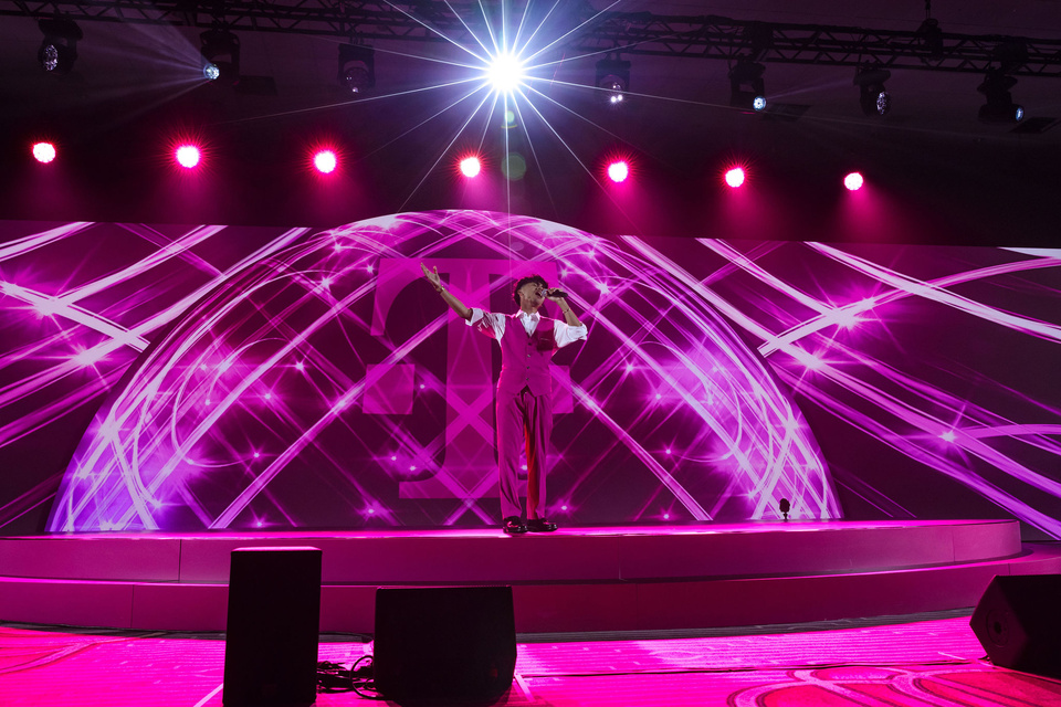 Photo of performer in a magenta suit singing on a stage in front of a magenta set with a T-Mobile logo