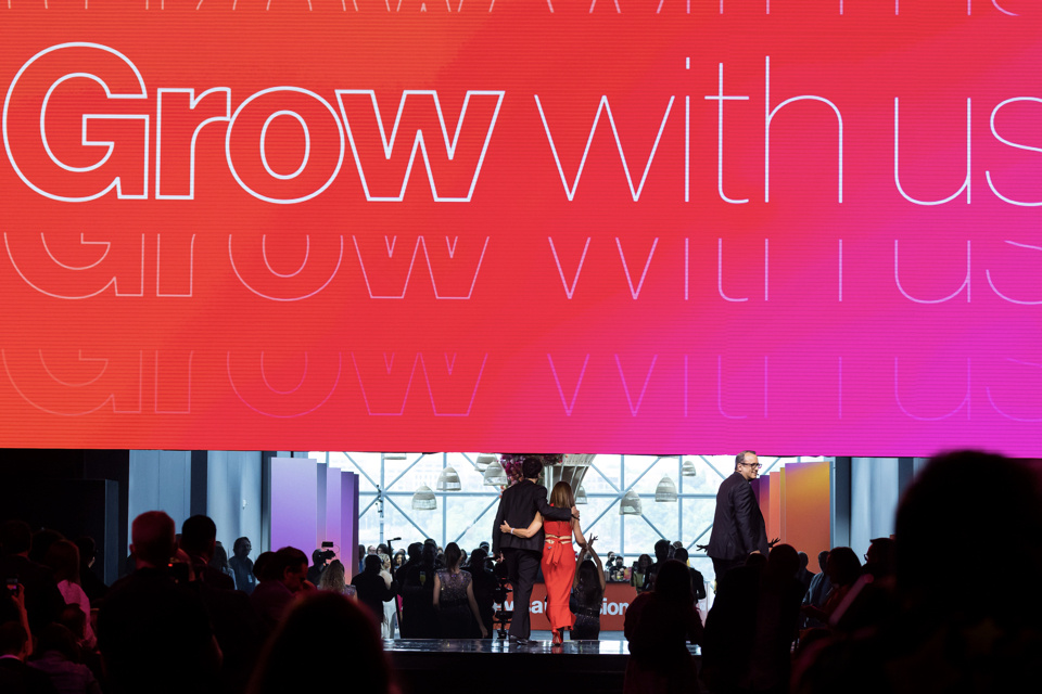 Photo of 2 performers walking off a stage as an LED screen pulls up with the text "Grow with us" on the screen