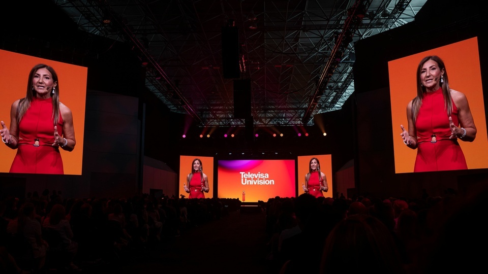 Photo of a woman speaking to an audience on a 5 Screen Stage. Center Screen has TelevisaUnivision Logo