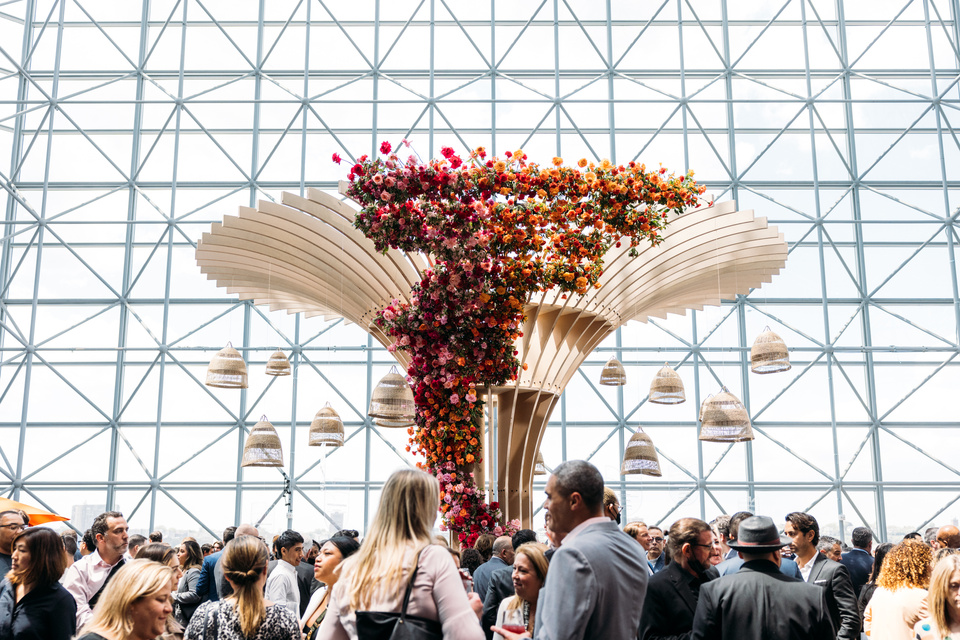 Photo of many event guests in a Reception Area with a floral Sculpture in the center.