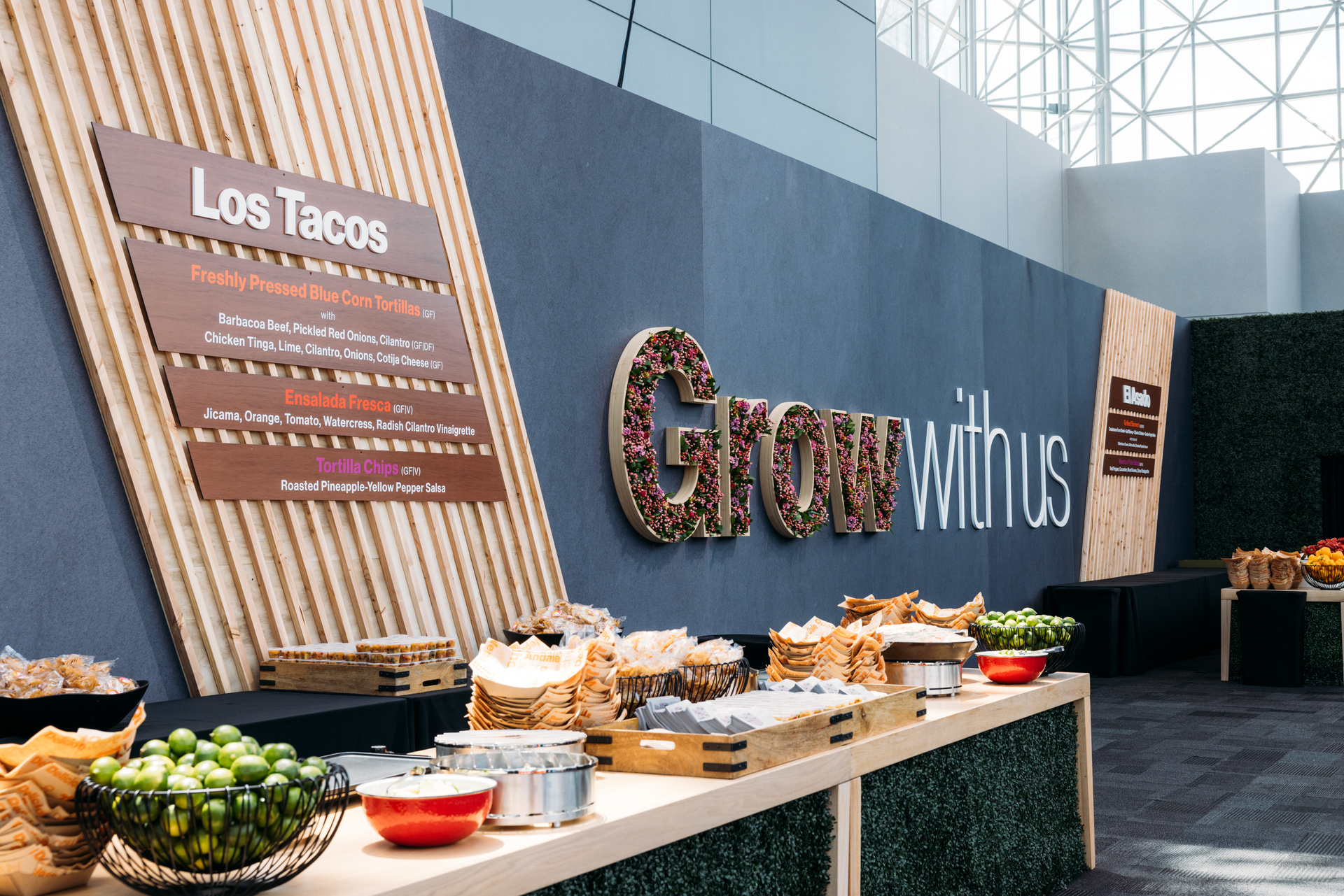 Photo of Food Laid Out on A Table, with signage reading "Grow with Us" and "Los Tacos"