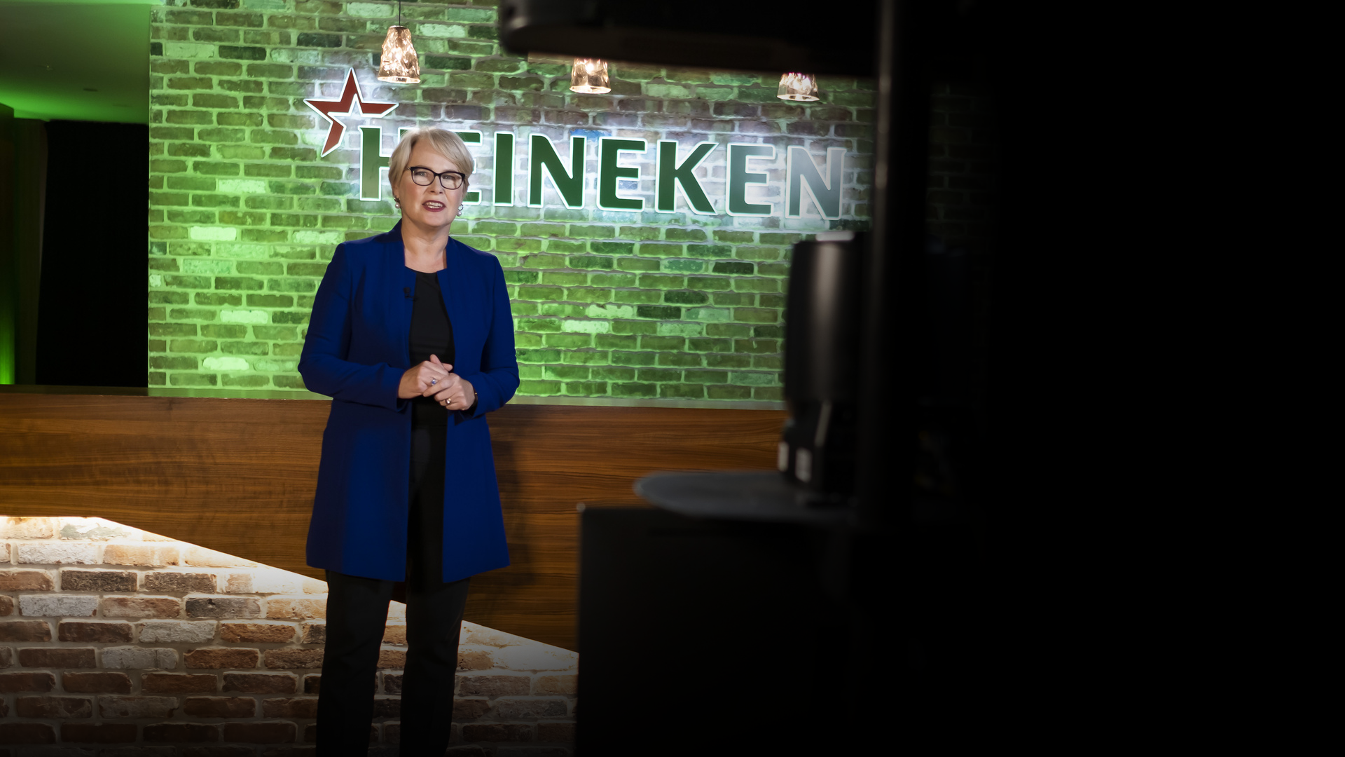 Photo of Heineken USA CEO speaking in front of green brick wall with Heineken logo