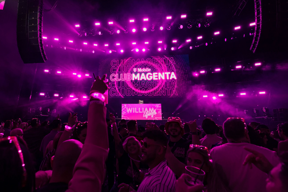 Image of Club Magenta attendees in crowd dancing to DJ who is performing in front of T-Mobile Club Magenta branding