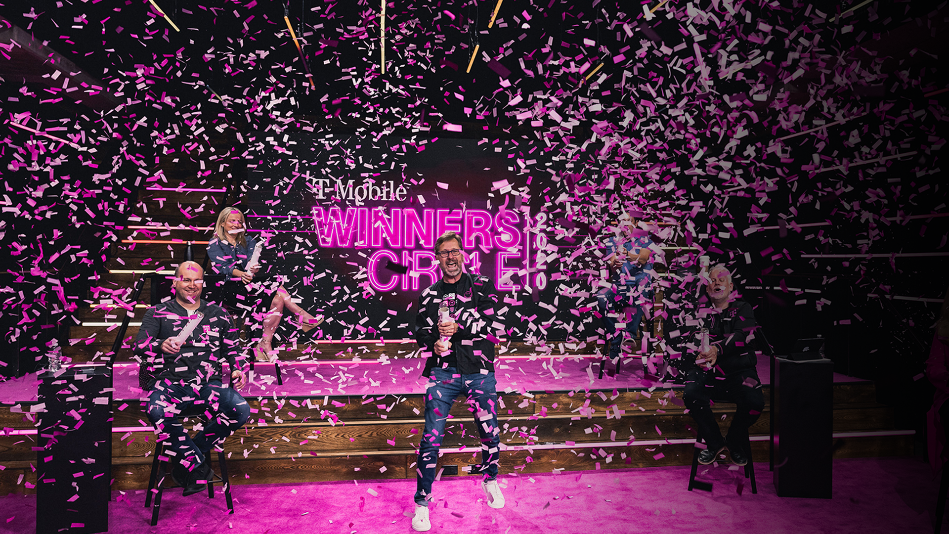 Photo of 6 people on stage shooting magenta confetti canons in front of a T-Mobile Winners Circle backdrop