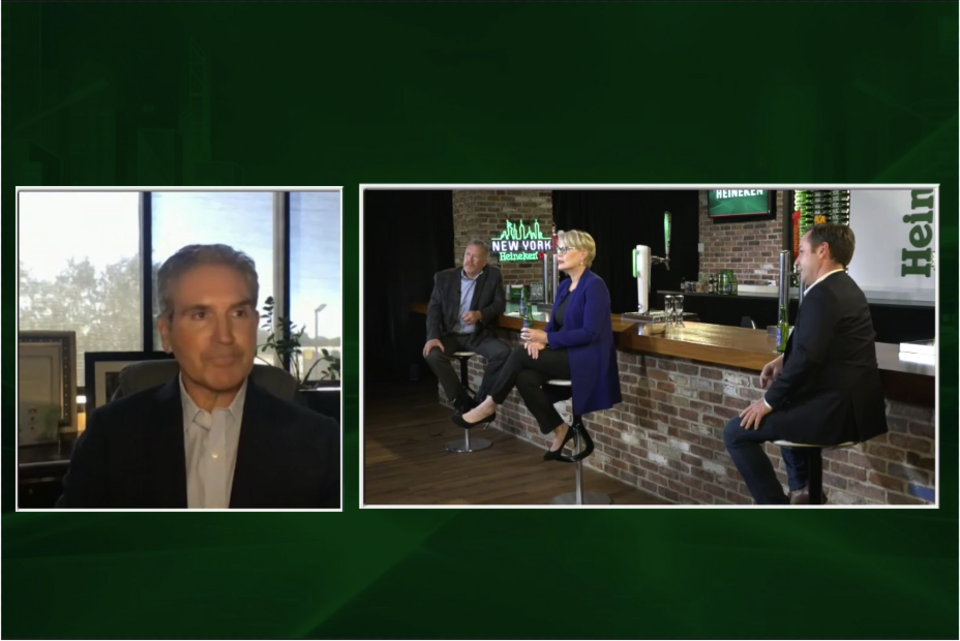 Screen shot of a Virtual meeting with one man on the right frame and three people on the left frame at a bar with Heineken branding on a Dark Green backdrop.