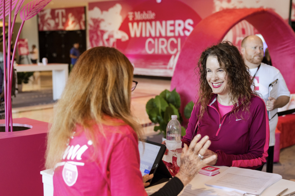 Photo of T-Mobile event staff member checking in an event guest with T-Mobile Winners Circle branding in a magenta setting