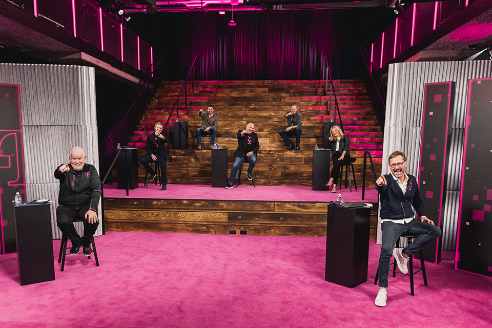 Photo of 7 people seated on a two-tier Magenta carpeted stage with T-Mobile Winner Circle 2020 displayed on a TV. People are pointing and smiling at the camera.