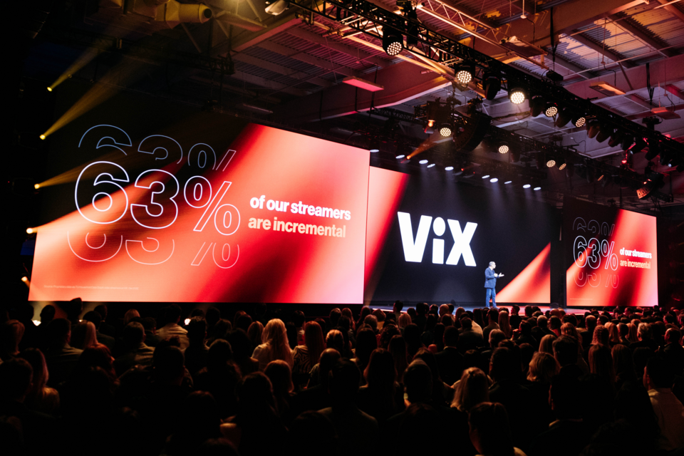 Photo of presenter on stage in front of Triple Screen Stage that reads "VIX: 63% of Our Streamers." Presenter is addressing the audience.