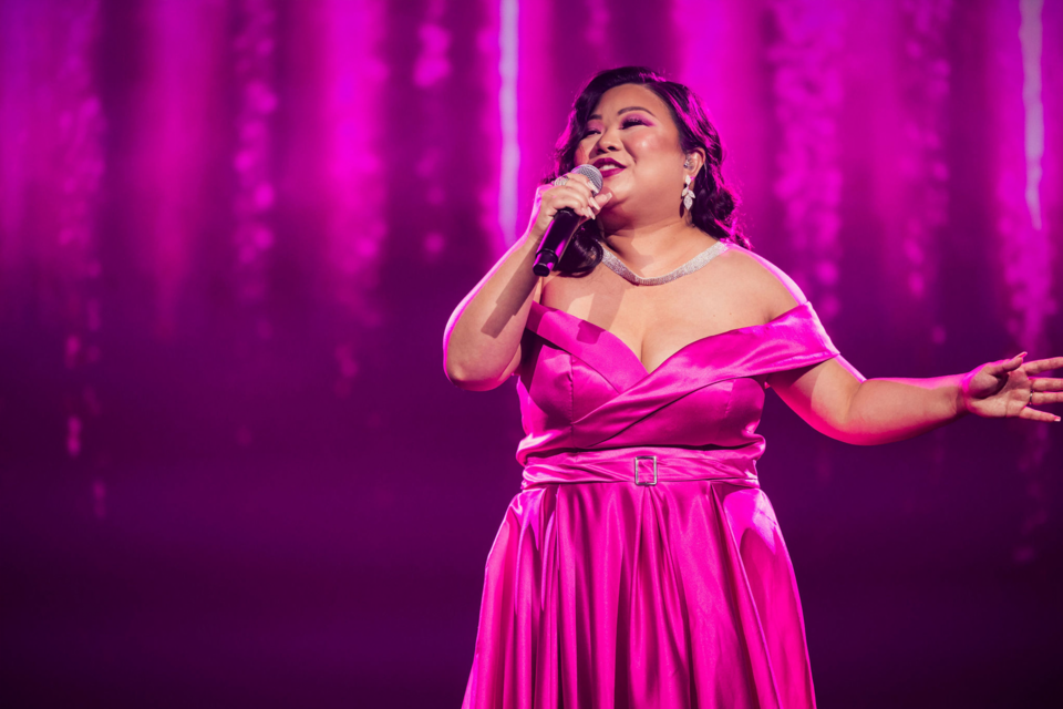 Photo of performer on stage signing while wearing a magenta dress